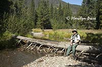 Carl sits on a log which crosses the Colorado River near its source, Colorado River Trail, Rocky Mountain National Park, CO