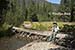 Carl sits on a log which crosses the Colorado River near its source, Colorado River Trail, Rocky Mountain National Park, CO